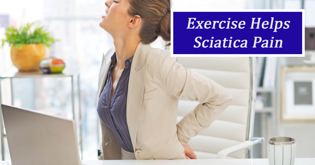 Exercises for Sciatica. Picture of a young caucasian female sitting at a desk at work and holding her lower back as if in pain.